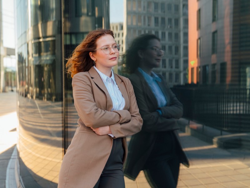 Nachdenkliche Geschäftsfrau stützte sich auf Bürogebäude mit Reflexion.