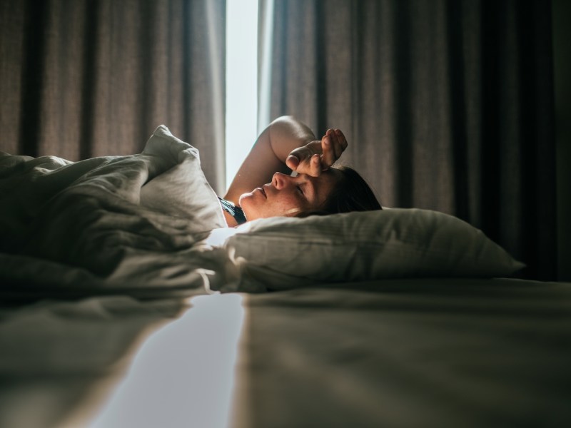 Eine Frau liegt im Bett und hält ihre Hand an die Stirn.