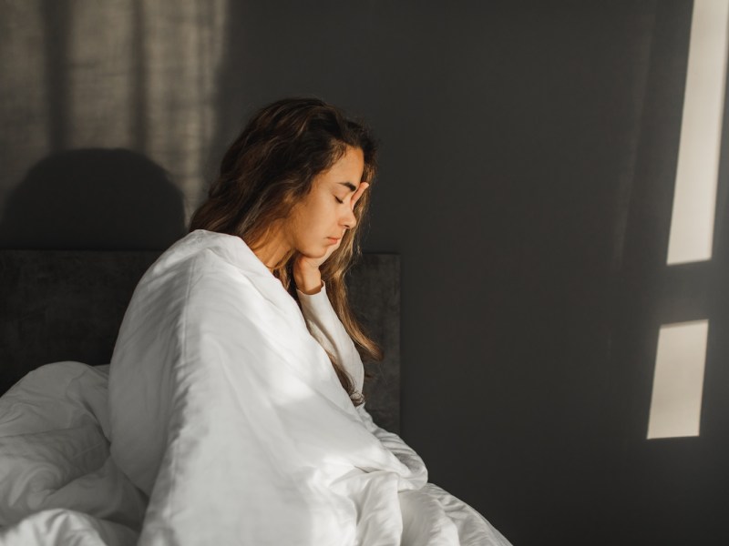 Frau sitzt krank auf der Bettkante.