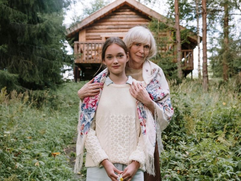 Oma und Enkelkind vor einer Hütte im Wald