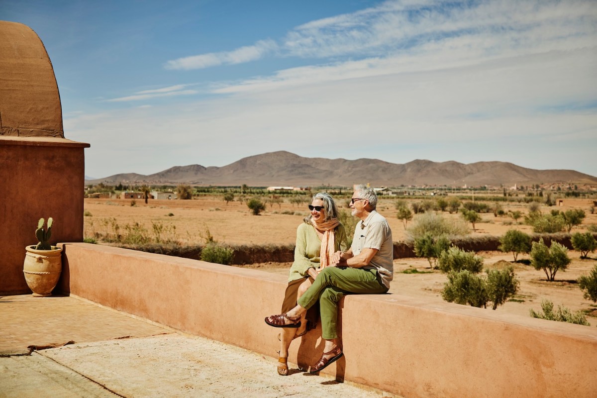 Weitwinkelaufnahme eines lächelnden Seniorenpaares, das während seines Urlaubs in Marokko auf der Dachterrasse eines Resorts entspannt.