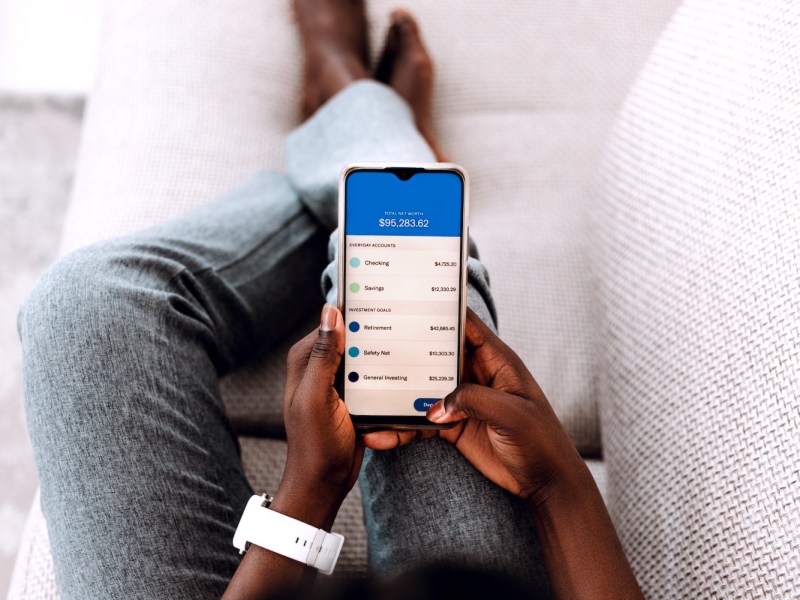 Eine junge schwarze Frau aus der Vogelperspektive erledigt Online-Banking-Aktivitäten mit ihrem Smartphone.