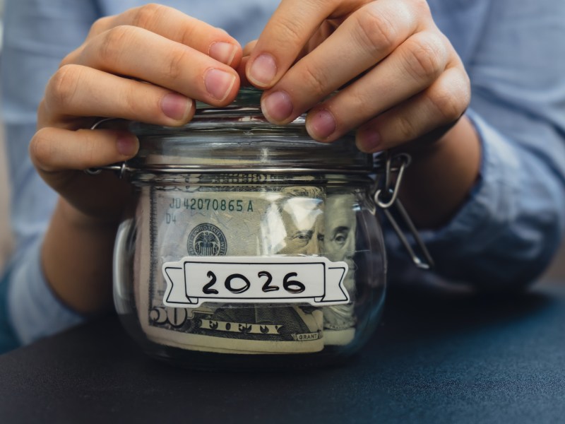 Female hands holding Glass jar full of American currency dollars cash banknote with text 2026 year. Preparation saving money. Moderate consumption and economy. Collecting money