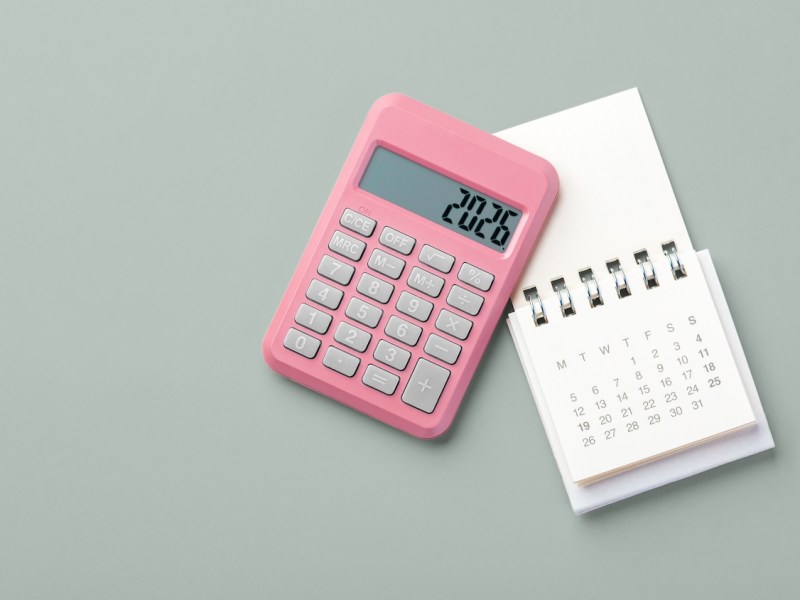 Pinkfarbener Taschenrechner mit der Jahreszahl 2026 und Kalender auf grünem Hintergrund.