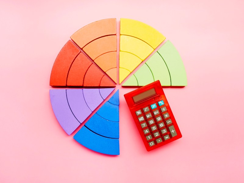 Draufsicht auf ein aus bunten Bausteinen bestehendes Tortendiagramm und einen roten Taschenrechner auf rosa Hintergrund.