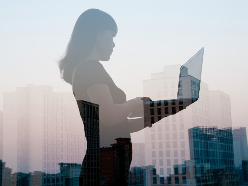 Doppelbelichtung einer Frau mit Laptop und Stadtlandschaft.