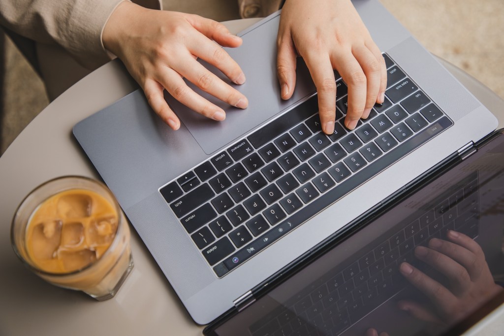 Draufsicht auf eine Frauenhand, die in einem Caf&eacute; einen Laptop benutzt.