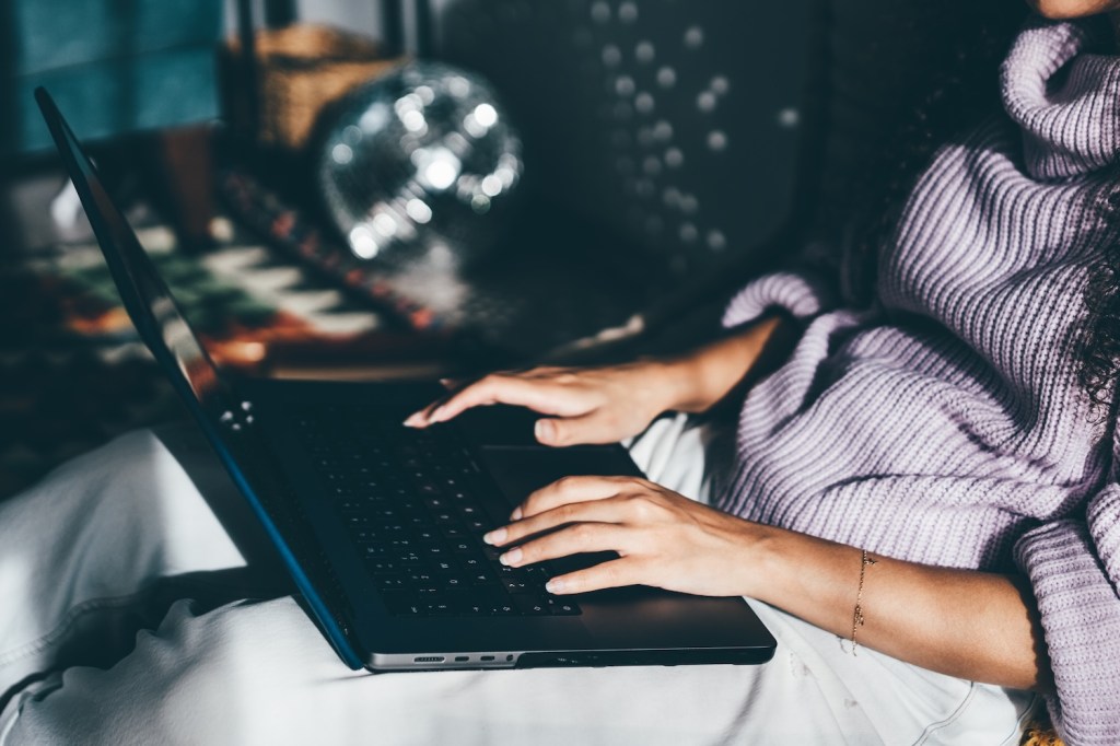 Junge Frau arbeitet mit Laptop im Wohnzimmer.
