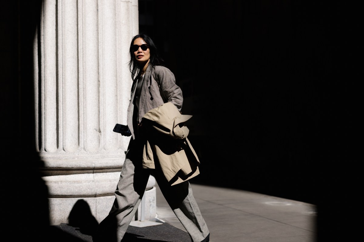 Eine stilvolle Geschäftsfrau schreitet selbstbewusst durch die Straßen der Stadt, den Trenchcoat lässig über den Arm geworfen.