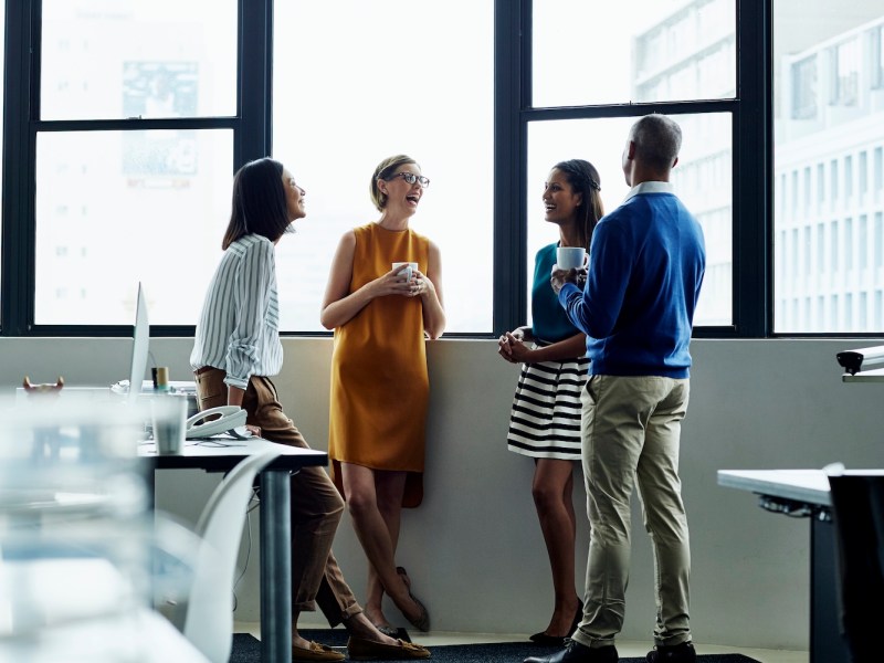Eine Gruppe von Mitarbeitenden steht im Büro und lacht.