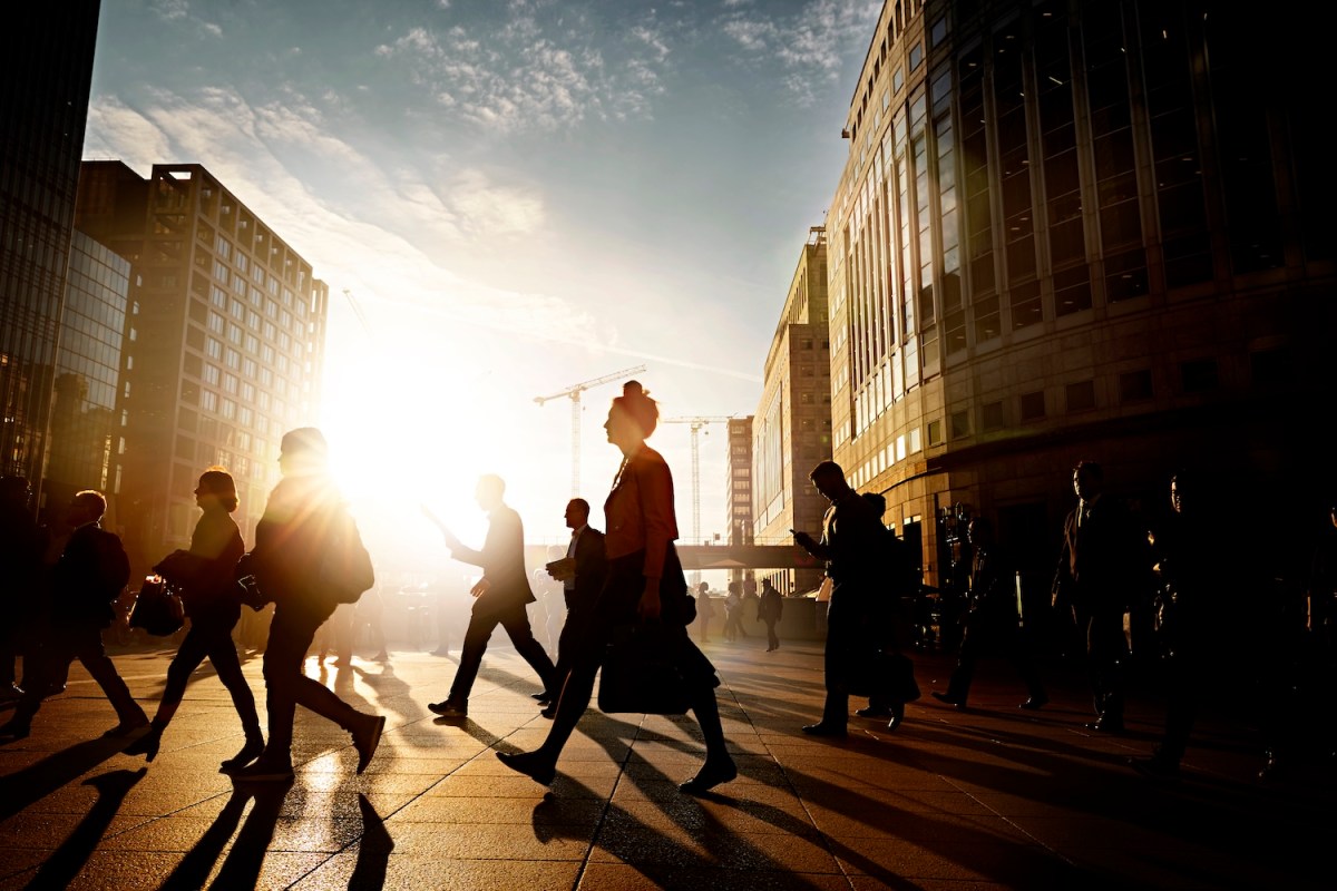 Eine Frau geht mit anderen Geschäftsleuten über die Straße.