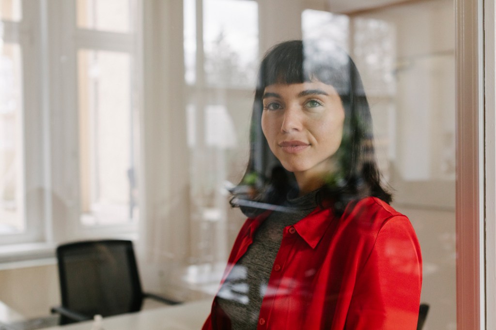 Das Portr&auml;t einer Gesch&auml;ftsfrau, die hinter einer Glasscheibe im B&uuml;ro arbeitet.