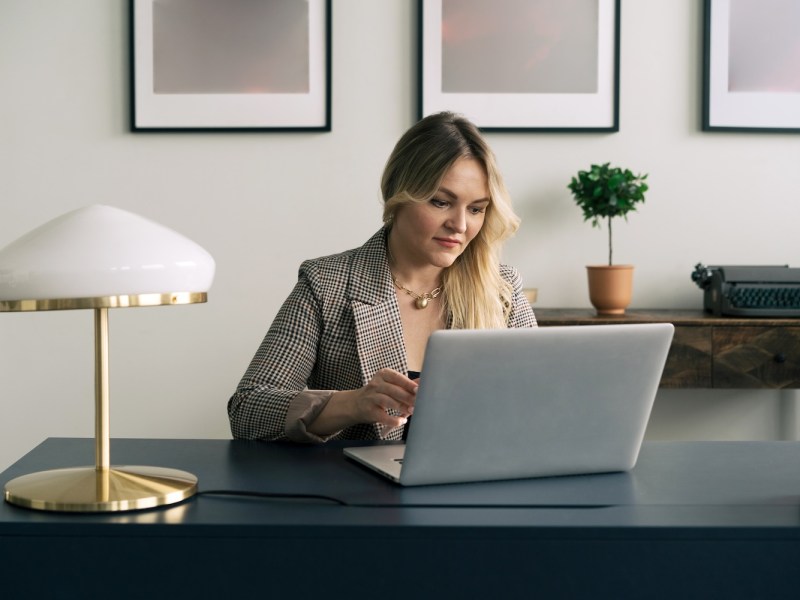 Eine blonde Frau sitzt am Laptop.