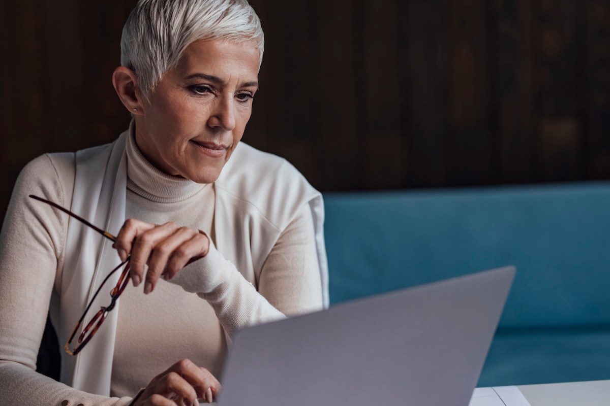 Eine ältere Dame mit grauen Haaren sitzt am Laptop.