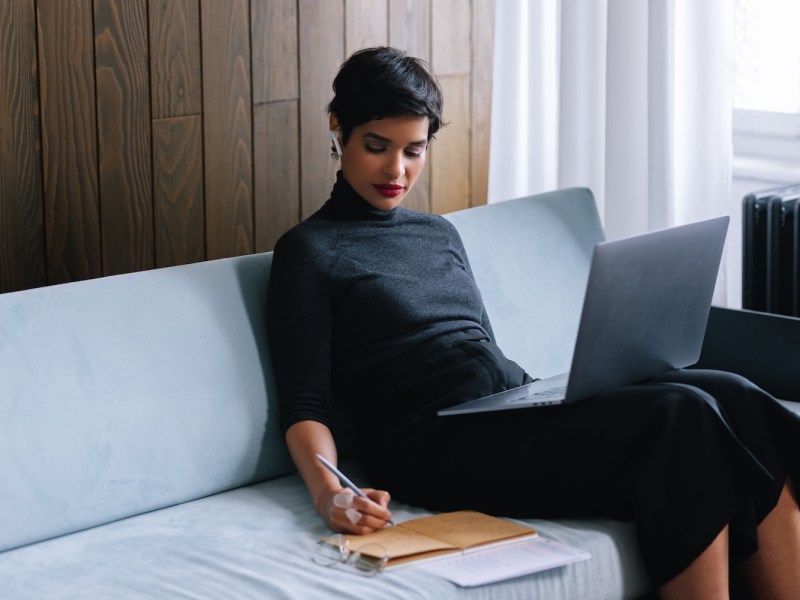 Frau sitzt auf einem Sofa und arbeitet an ihrem Laptop.