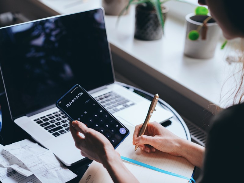 Frau sitzt vor dem Laptop mit Taschenrechner