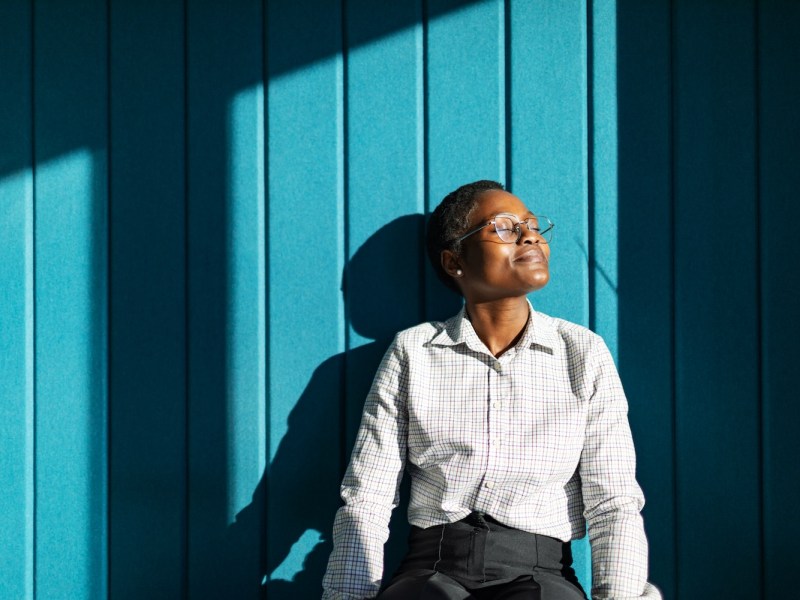 Eine junge, schwarze Frau sitzt lächelnd und entspannt in ihrem Büro.