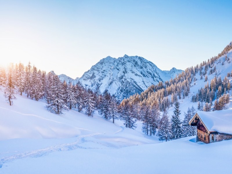 Panoramablick auf eine wunderschöne Winterlandschaft mit Bergmotiven und einer traditionellen Berghütte im Hintergrund in den Alpen im goldenen Abendlicht bei Sonnenuntergang.
