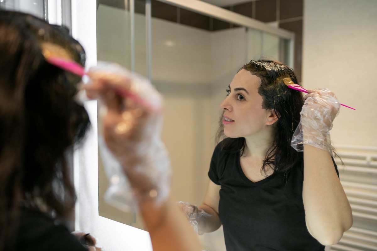 Frau färbt sich vor dem Spiegel selbst die Haare mit dm Haarfarbe