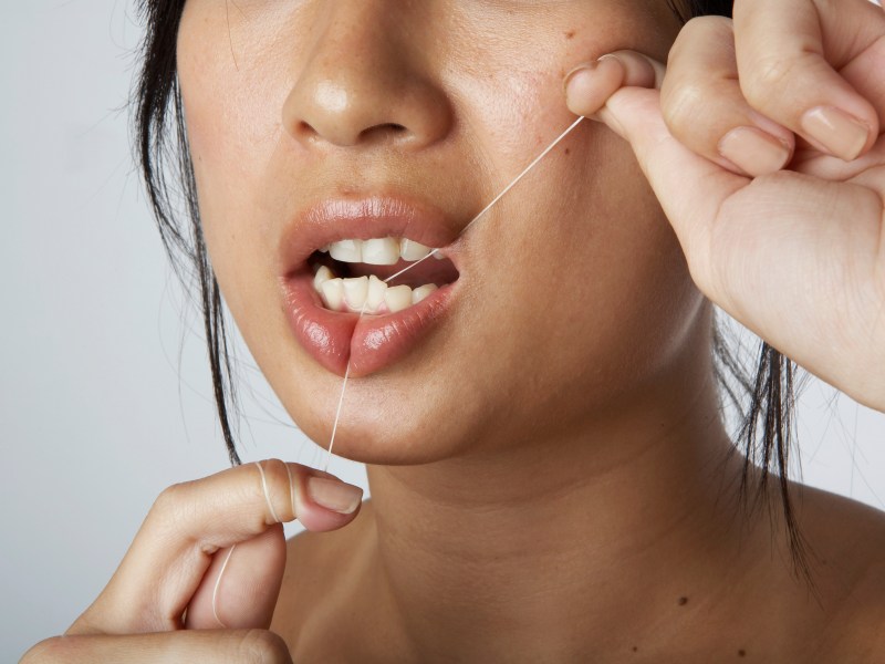 Frau benutzt Zahnseide