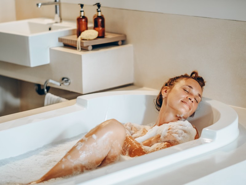 Frau liegt in der Badewanne mit Duschschaum